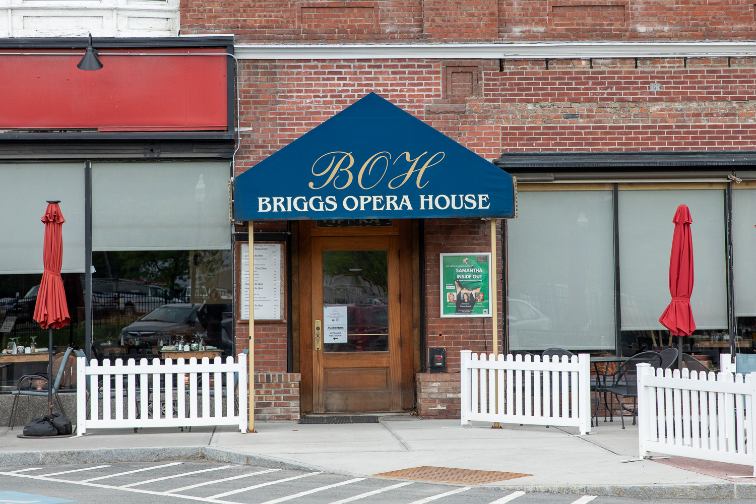 The view from the street of the front of a brick building with a blue awning with the words 'Briggs Opera House'