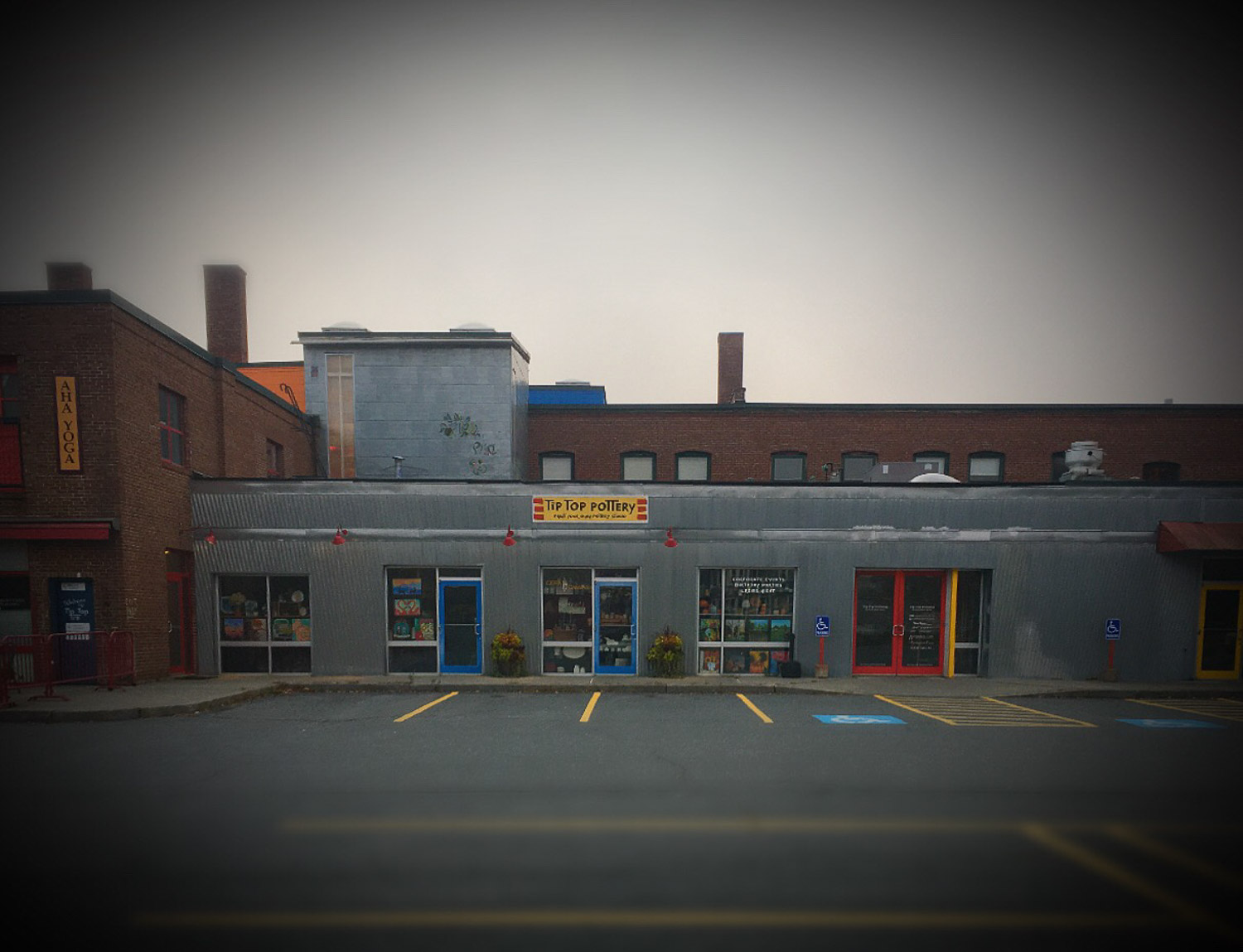 Screenshot The view from the street of a brick and metal building with a red front door and a yellow sign that says 'tip top pottery'